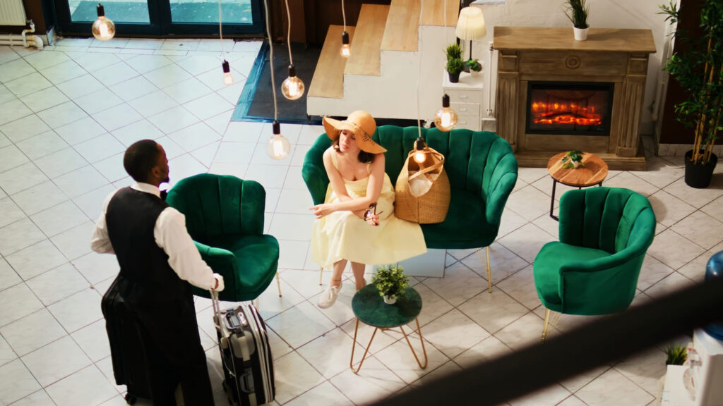 bellhop offering services woman lounge area waiting room check seaside hotel tourist sitting couch talking hotel concierge summer clothes handheld shot 1 1